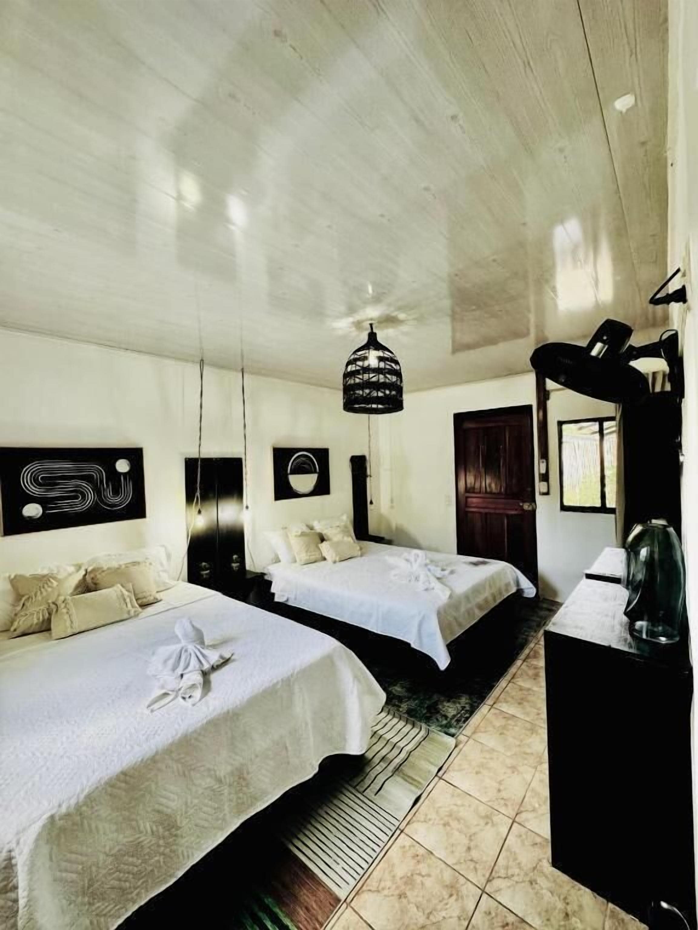 A hotel room with two beds, a ceiling light fixture, a desk with a lamp, and a wall-mounted mirror.