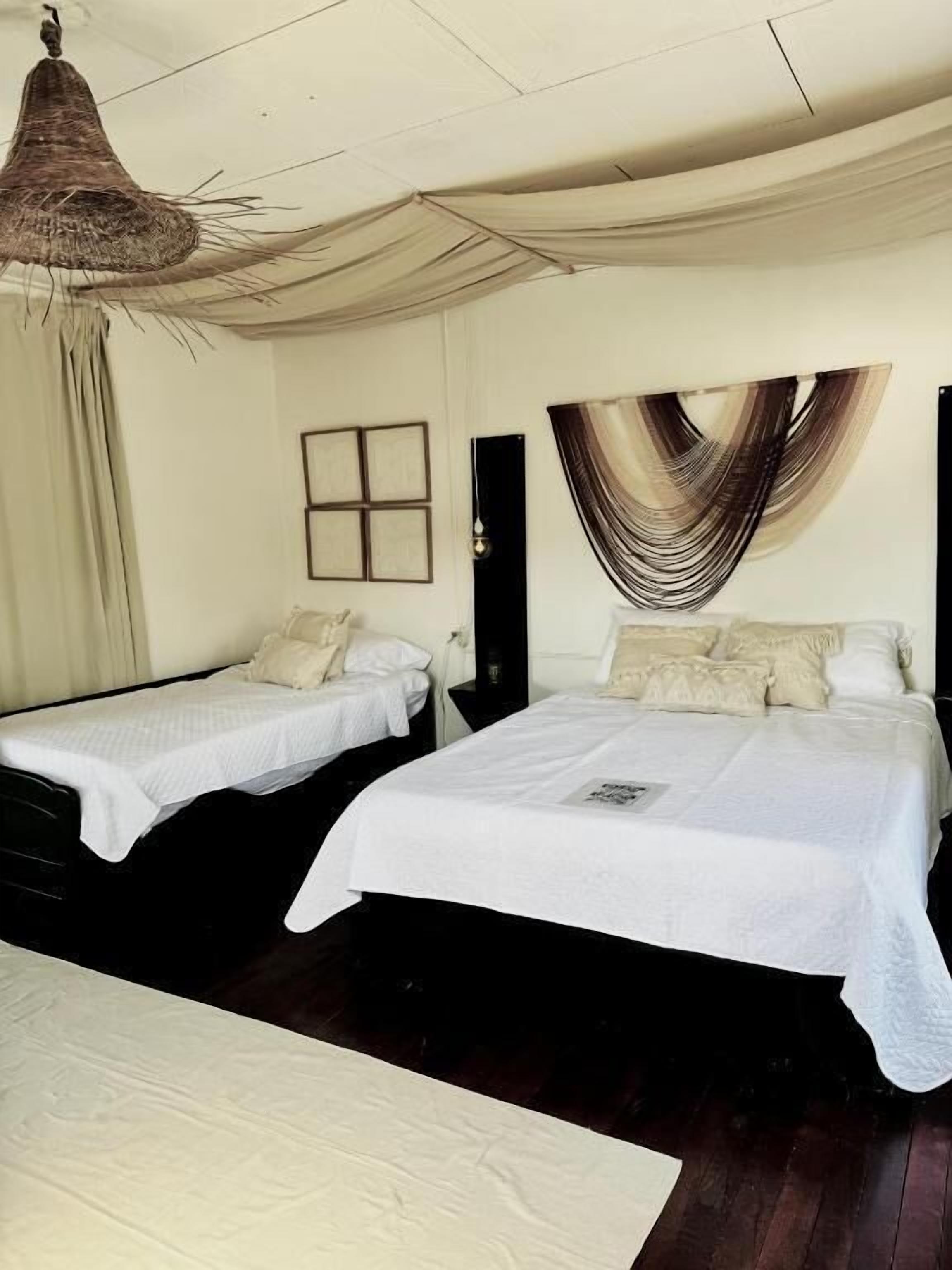 A hotel room with two beds, a hanging light fixture, a wall-mounted picture frame, and a draped curtain.