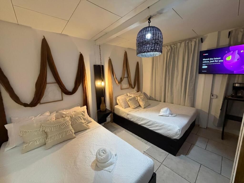Habitación de hotel con dos camas, un televisor y una lámpara colgante.