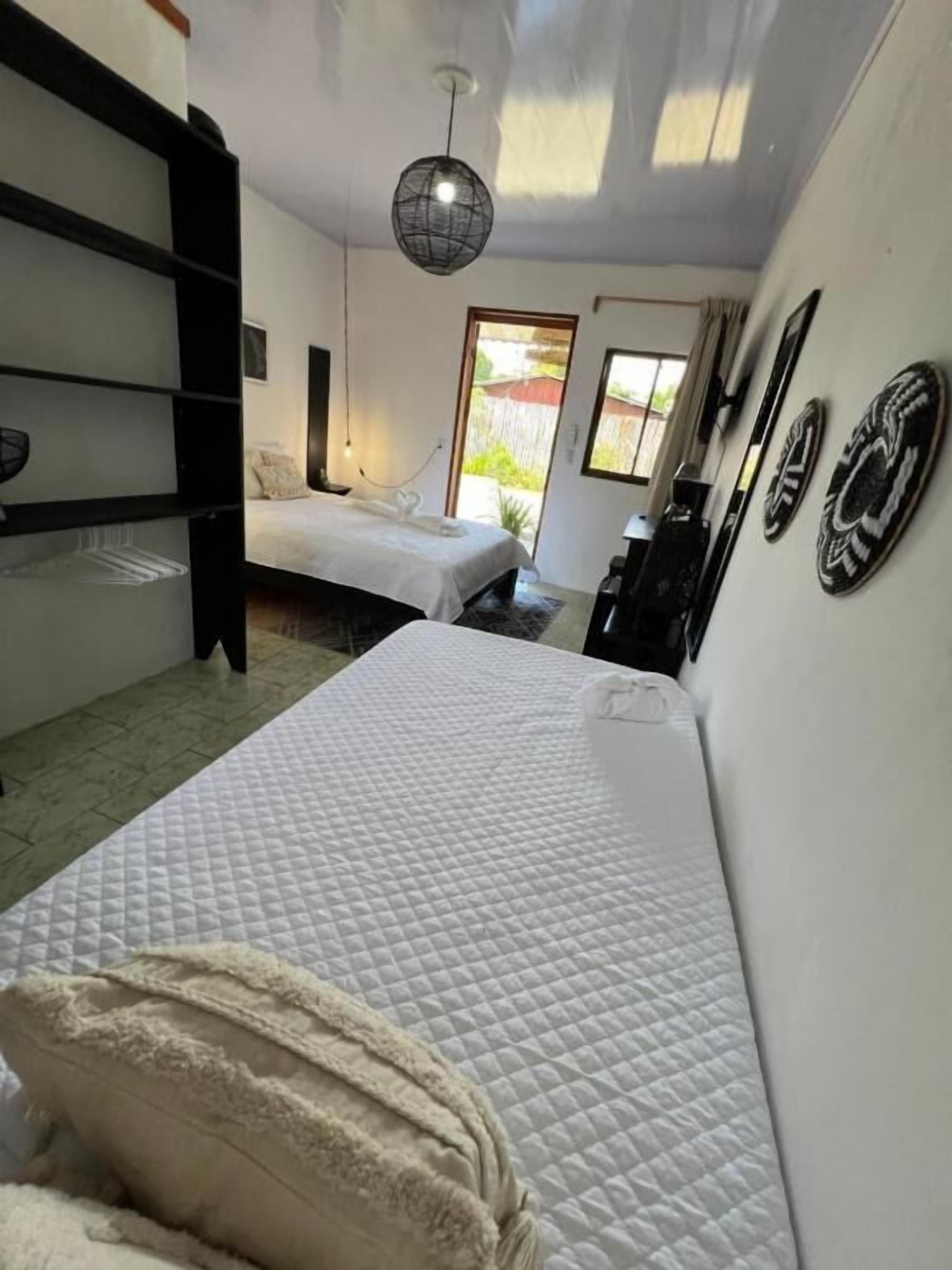 Ein Schlafzimmer mit Bett, einer Hängelampe, einem Kleiderschrank und Blick durch eine Tür.