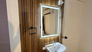 Un baño con pared de paneles de madera, un lavabo blanco, un espejo y un taburete pequeño.