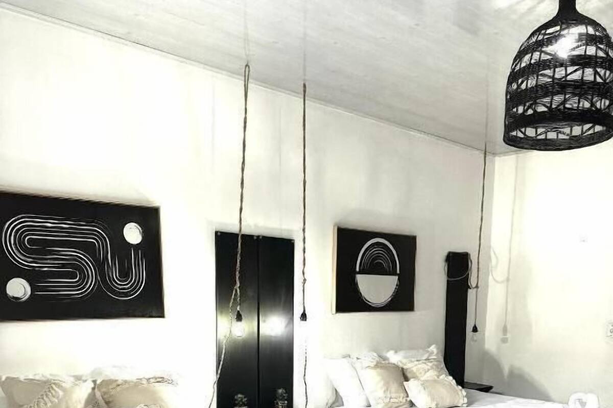 Un dormitorio con cama, mesita de noche, lámpara colgante y una obra de arte en la pared.