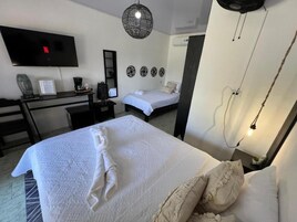 Una habitación de hotel con cama, escritorio, televisor y estante en la pared.