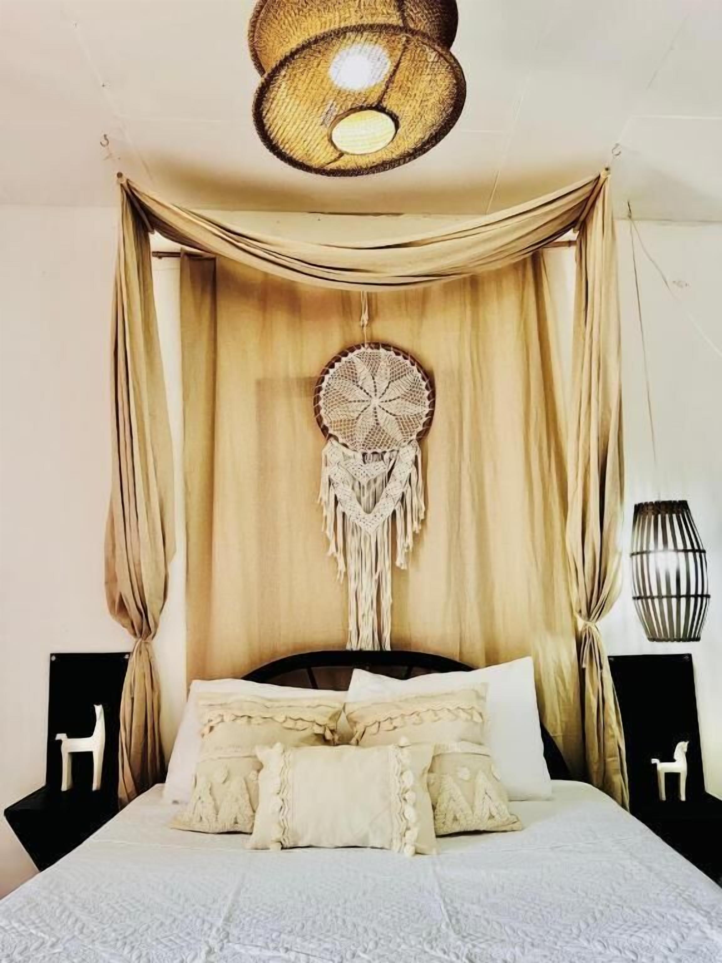A bed with a canopy, a macrame dreamcatcher, and a hanging light fixture.