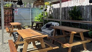 Un espacio al aire libre con mesas de picnic de madera y bancos, una lámpara colgante de mimbre y una valla de bambú.