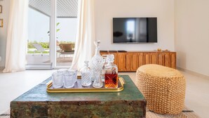 Un salon avec une table basse dont le plateau est en verre, un pouf en osier et un téléviseur fixé au mur.
