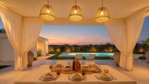 Un espace de restauration en plein air avec une table dressée pour un repas, entouré de rideaux blancs et illuminé par des lampes suspendues.