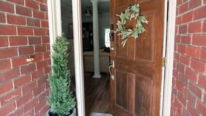 A wooden door with a wreath, a potted plant, and a brick wall.