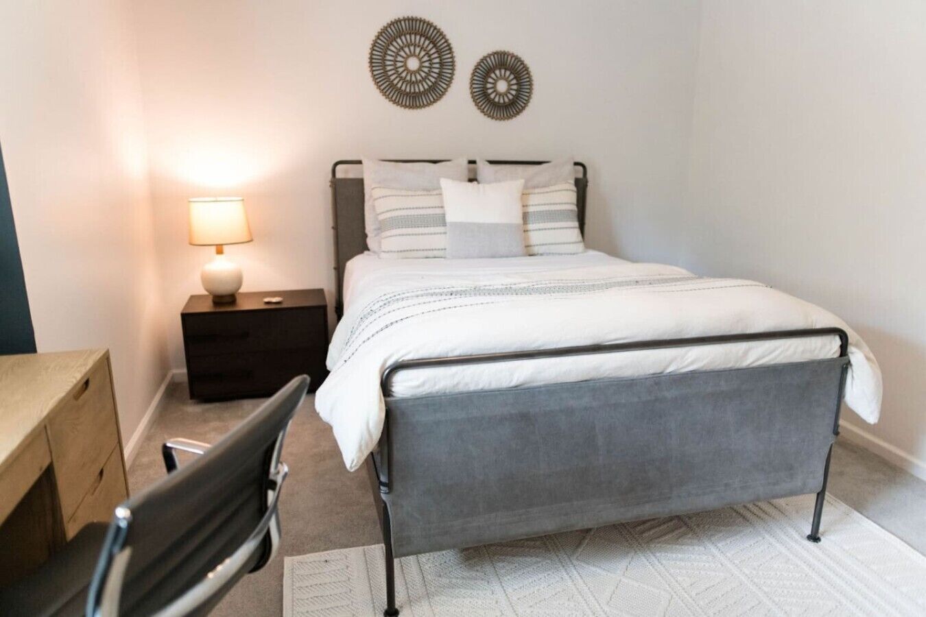 Un dormitorio con cama, mesita de noche, lámpara, silla y decoración mural.