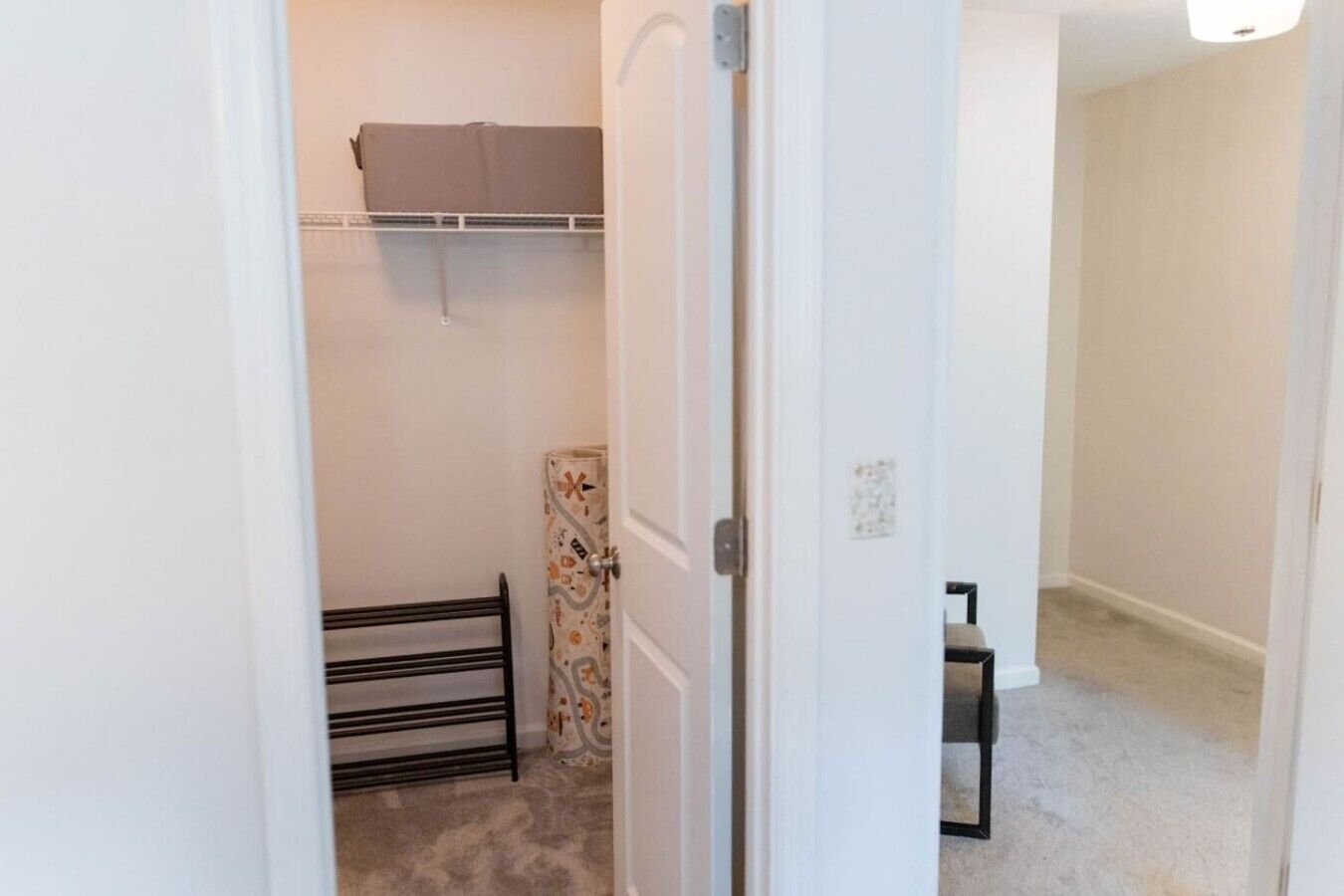 A hallway with a door leading to a room, a coat rack, a patterned rug, and a bench.