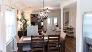 A dining area with a wooden table, chairs, a hanging light fixture, and a view into the living room.