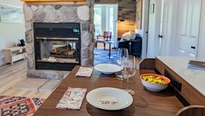 A dining table with plates, a bowl, and a wine glass in a room with a stone fireplace, a sofa, and a door. - Cozy Cabin - walk to creek - Close to Sedona (Rimrock)