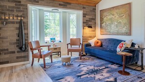 A room with a brick wall, wooden ceiling, a blue sofa, a wooden chair, a small table, and a rug. - Cozy Cabin - walk to creek - Close to Sedona (Rimrock)