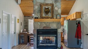 A stone fireplace with a framed animal head, wooden cabinets, a refrigerator, and a door with a sign. - Cozy Cabin - walk to creek - Close to Sedona (Rimrock)