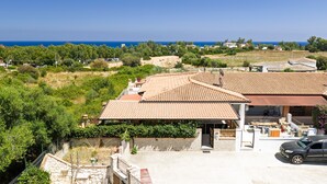 Une propriété située sur la côte, avec des toits recouverts de tuiles en terre cuite, un mur en pierre et une vue sur la mer.