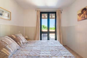 Un dormitori amb un llit, una cadira, una finestra amb cortines i un quadre al mur.