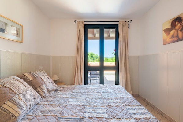 Une chambre à coucher avec un lit, une chaise, une fenêtre avec des rideaux et un tableau au mur.