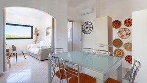 Un salon moderne avec une table à manger au plateau en verre, un canapé et une vue sur l’extérieur.
