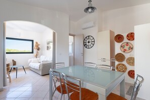 Un salon moderne avec une table à manger au plateau en verre, un canapé et une vue sur l’extérieur.