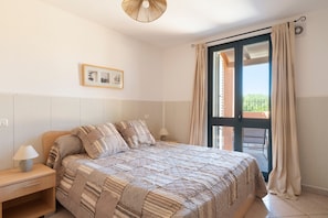 Une chambre à coucher avec un lit, une table de chevet, une lampe et une fenêtre avec des rideaux.