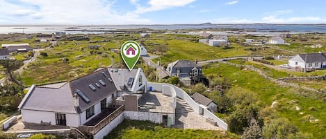 A coastal property with a prominent house featuring a curved roof, a stone wall, and a small deck.