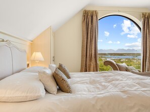 Ein Schlafzimmer mit einem großen Bett, einem Nachttisch, einer Lampe und einem Fenster mit Vorhängen.