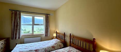 A room with two beds, a window with curtains, a radiator, and a lamp on a bedside table.