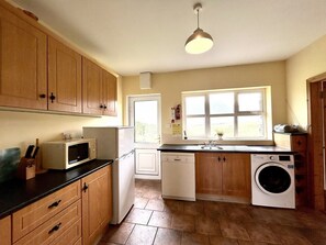 A compact kitchen with wooden cabinets, a microwave, a dishwasher, and a washing machine. - Twelve Bens Lodge (Recess)