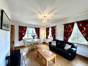 A furnished living room with a black leather sofa, wooden coffee table, and a dining area with a table and chairs. - Twelve Bens Lodge (Recess)