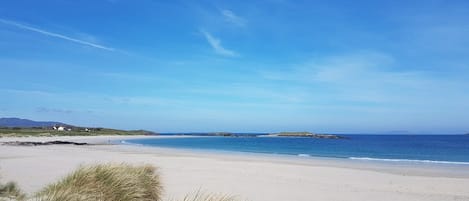 Una playa con cielos despejados, orilla arenosa y formaciones terrestres a lo lejos.