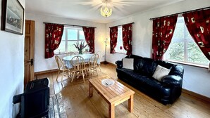 Un salon avec une table basse en bois, un canapé en cuir noir, une table à manger avec des chaises et des rideaux rouges.