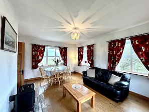 Ein Wohnzimmer mit Couch aus schwarzem Leder, einem Holztisch, einem Esstisch mit Stühlen und roten Vorhängen.