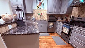 Une cuisine moderne avec des meubles gris, un plan de travail en granit, un four encastré et un plancher en bois.