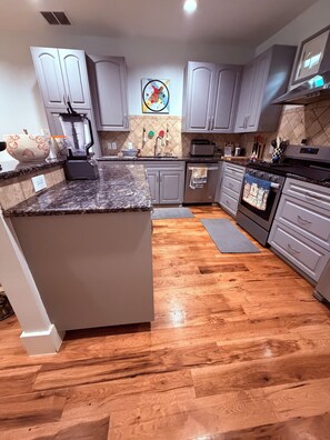 Eine moderne Küche mit grauen Schränken, einer Granit Arbeitsplatte, einem eingebauten Backofen und Holzboden.