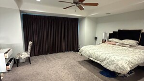 Une chambre à coucher avec un lit, une chaise, un ventilateur de plafond et une fenêtre avec des rideaux.