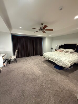 Ein Schlafzimmer mit einem Bett, einem Sessel, einem Deckenventilator und einem Fenster mit Vorhängen.