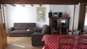 Un salon avec un canapé, une table à manger recouverte d’une nappe à pois et un meuble contenant des haut-parleurs.