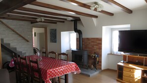 Un coin repas avec une nappe rouge, des chaises en bois, une cheminée, un téléviseur posé sur un meuble en bois et un escalier menant à l’étage.