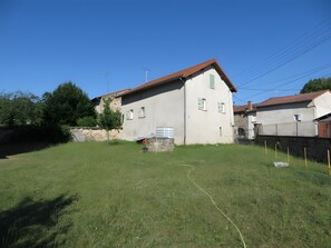 A two-story building with a sloped roof, a stone wall, and a grassy yard.