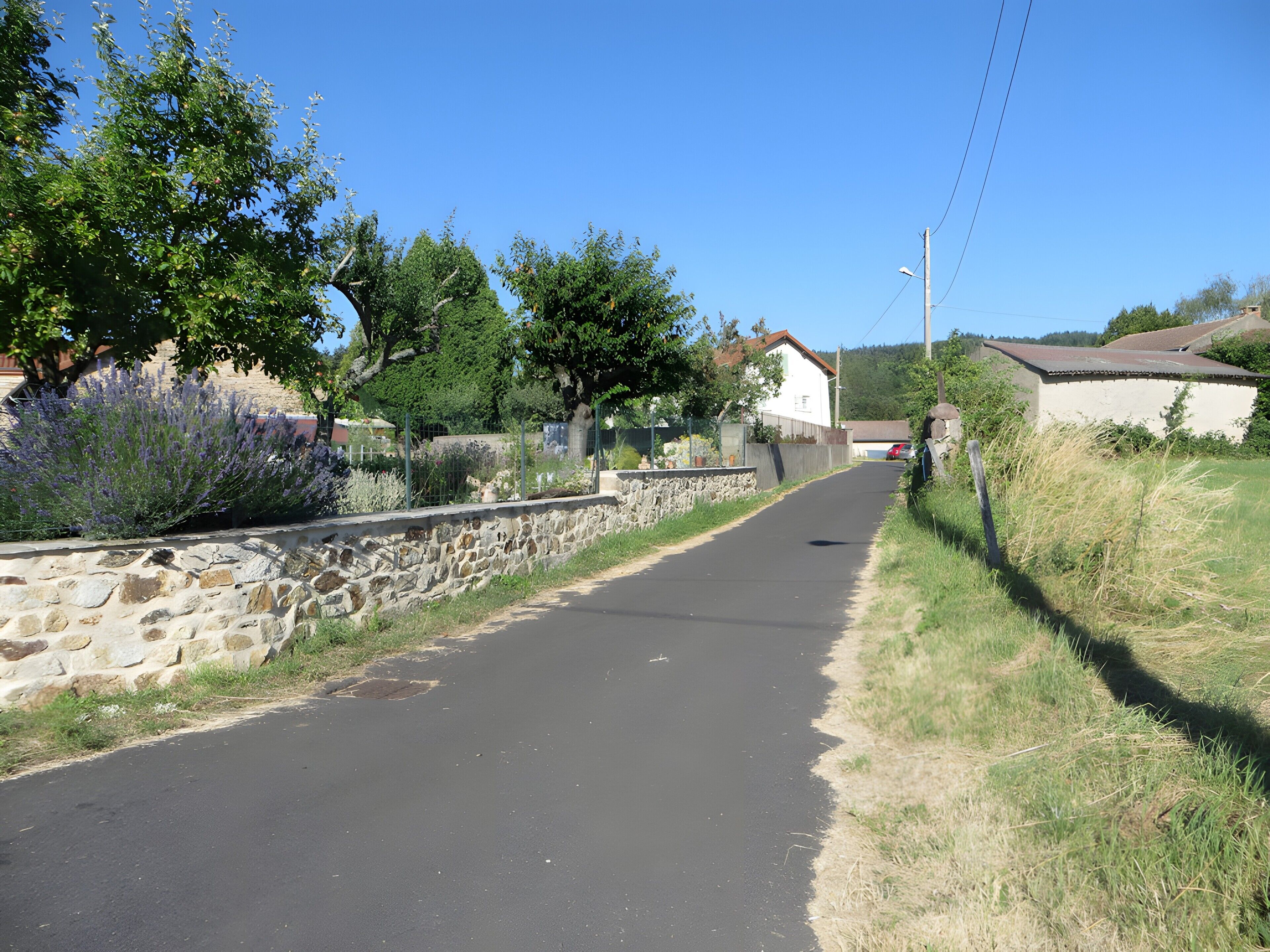 Une route pavée, bordée de murs de pierre et de végétation, qui mène à un bâtiment blanc coiffé d’un toit rouge.