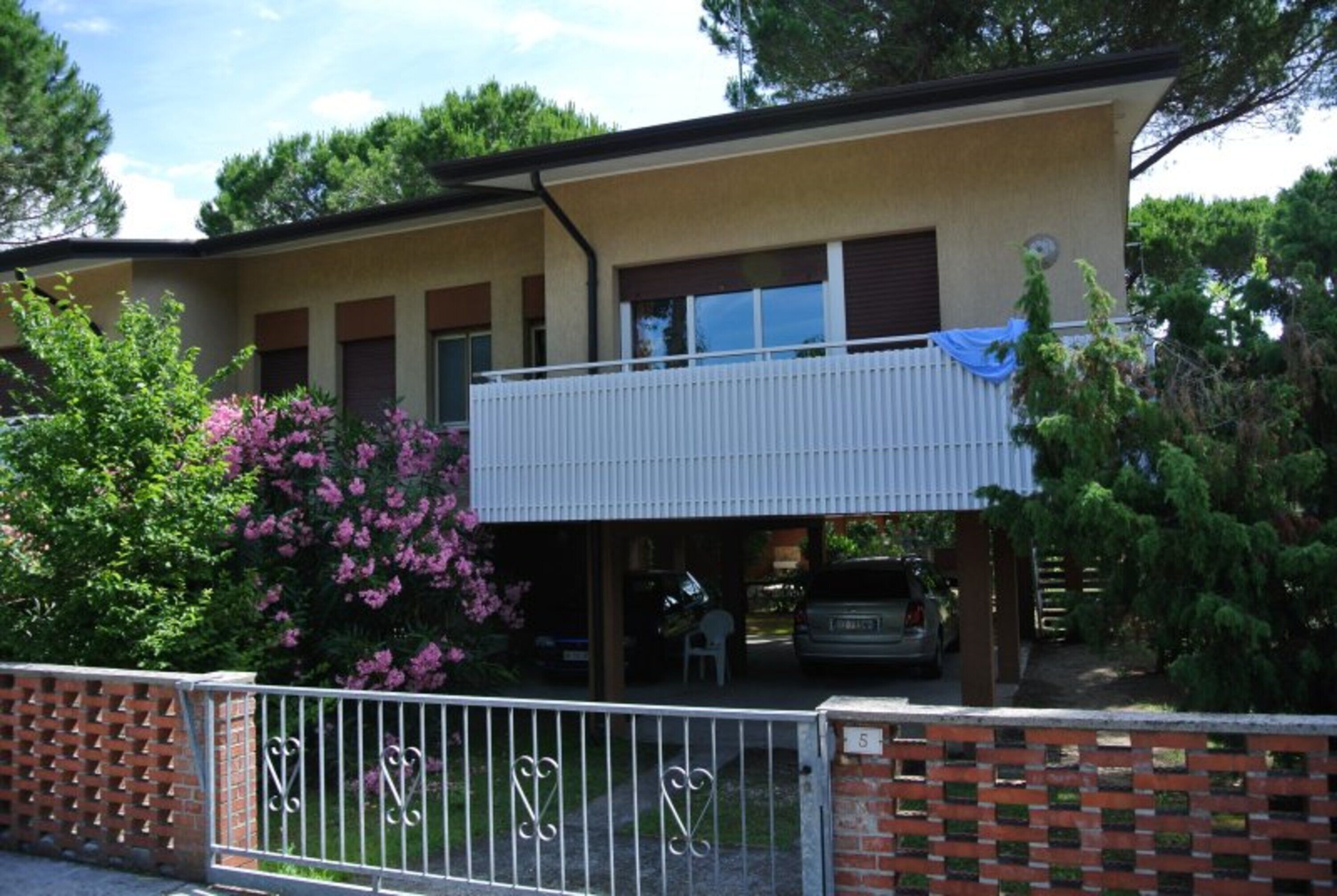 A two-story building with a balcony, a covered parking area, and a fenced garden.