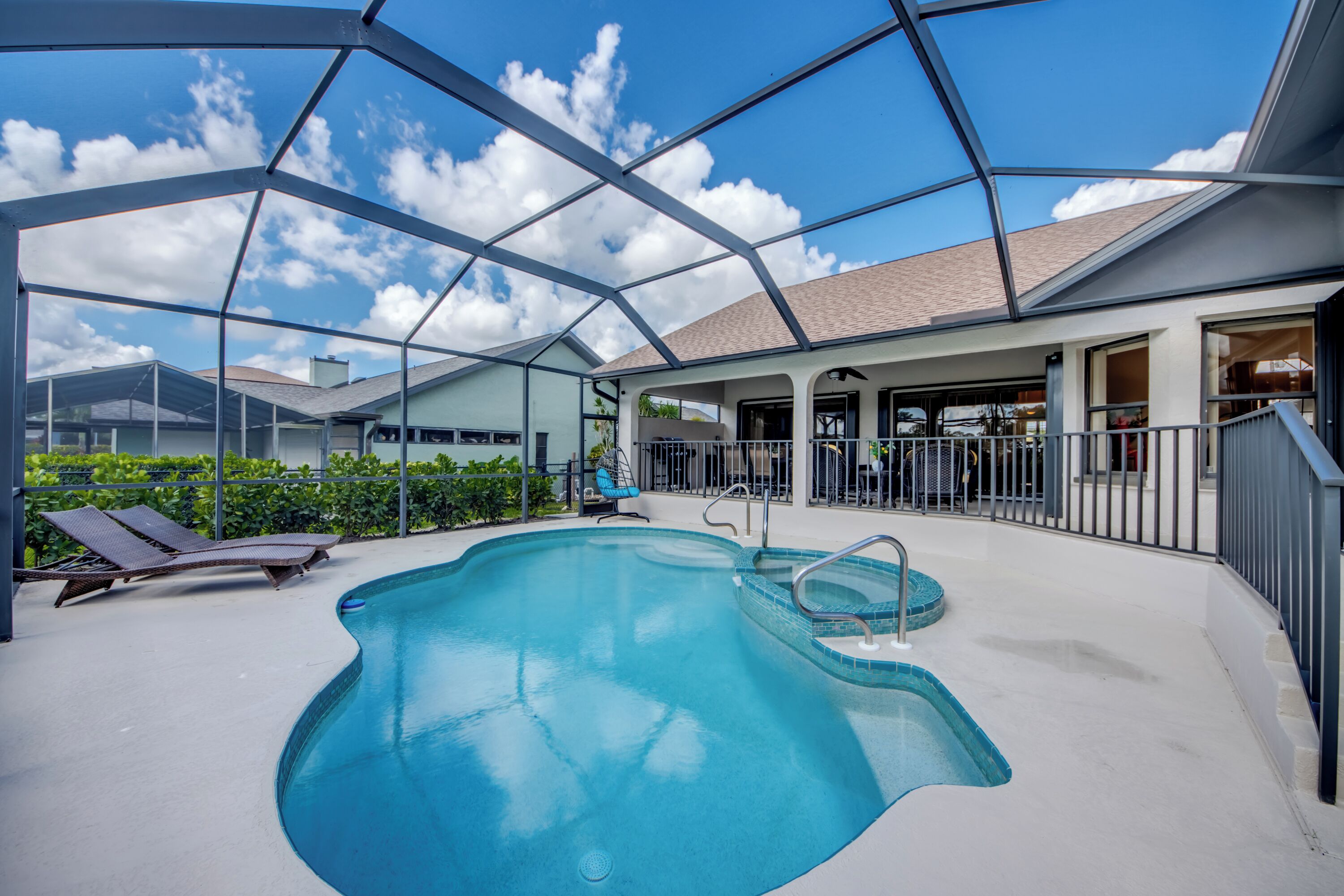 Una piscina con cerramiento de vidrio, sillas de descanso y un área de patio techada.
