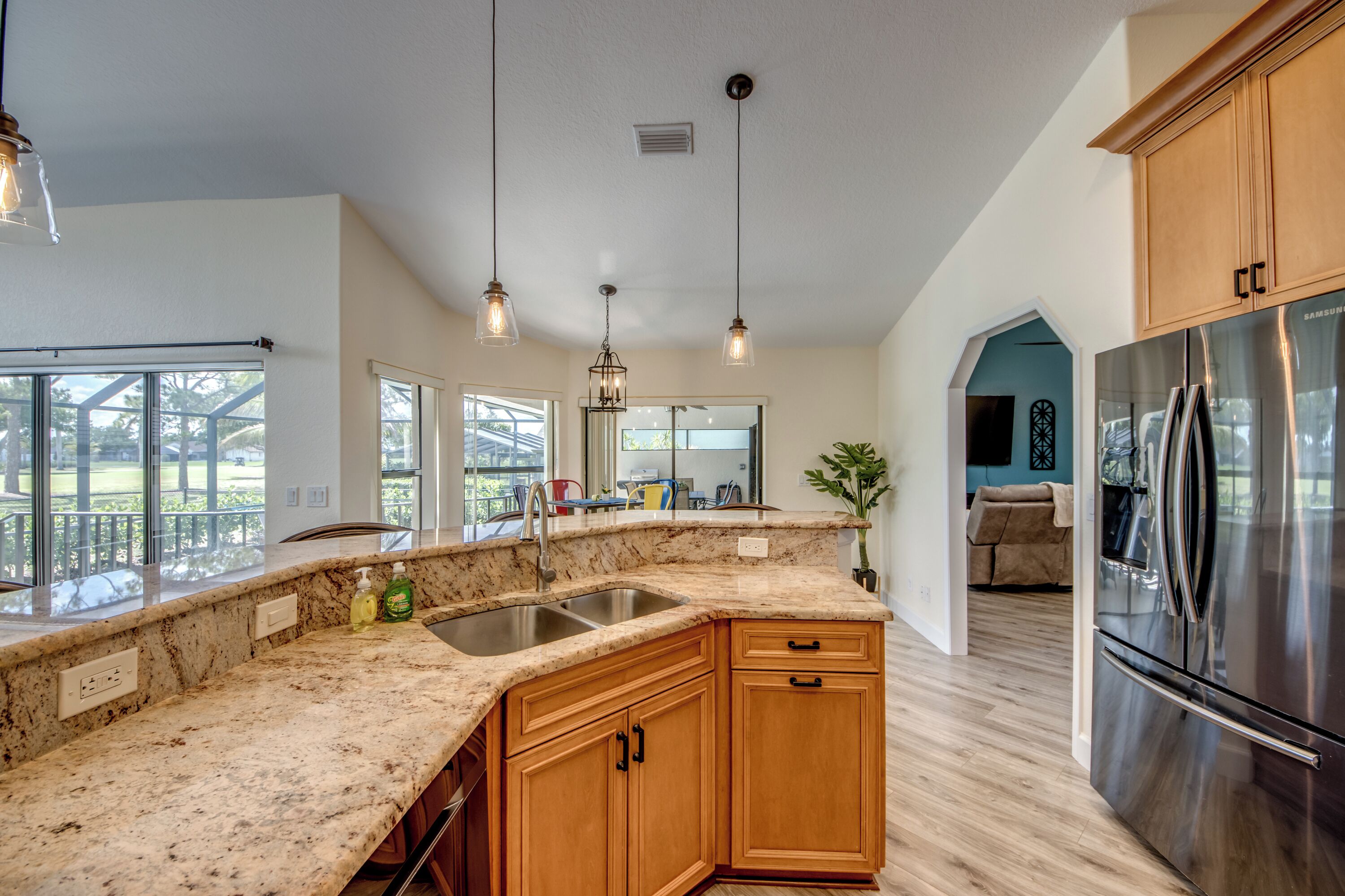 A kitchen with granite countertops, wooden cabinets, stainless steel appliances, pendant lighting, and a large window.
