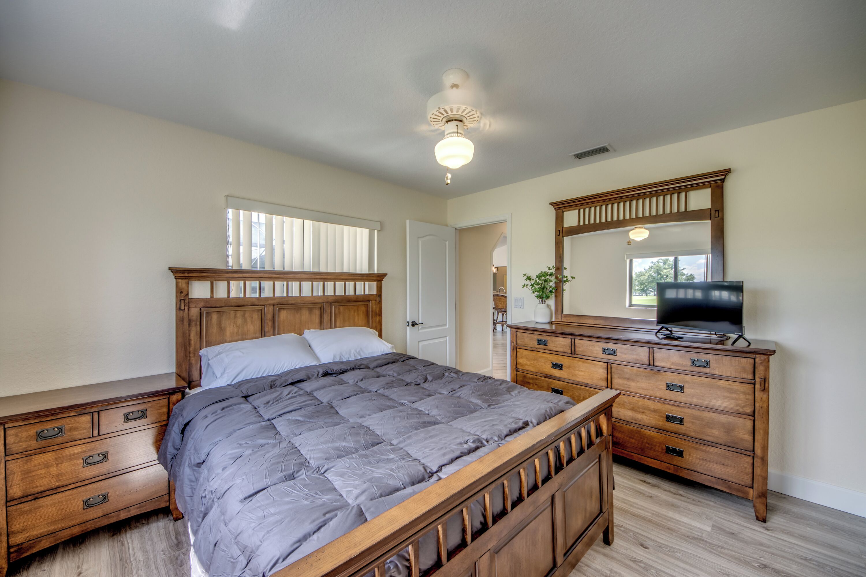 A bedroom with a wooden bed, a dresser, a television, and a ceiling fan.