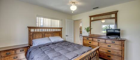 A bedroom with a wooden bed, a dresser, a television, and a ceiling fan.