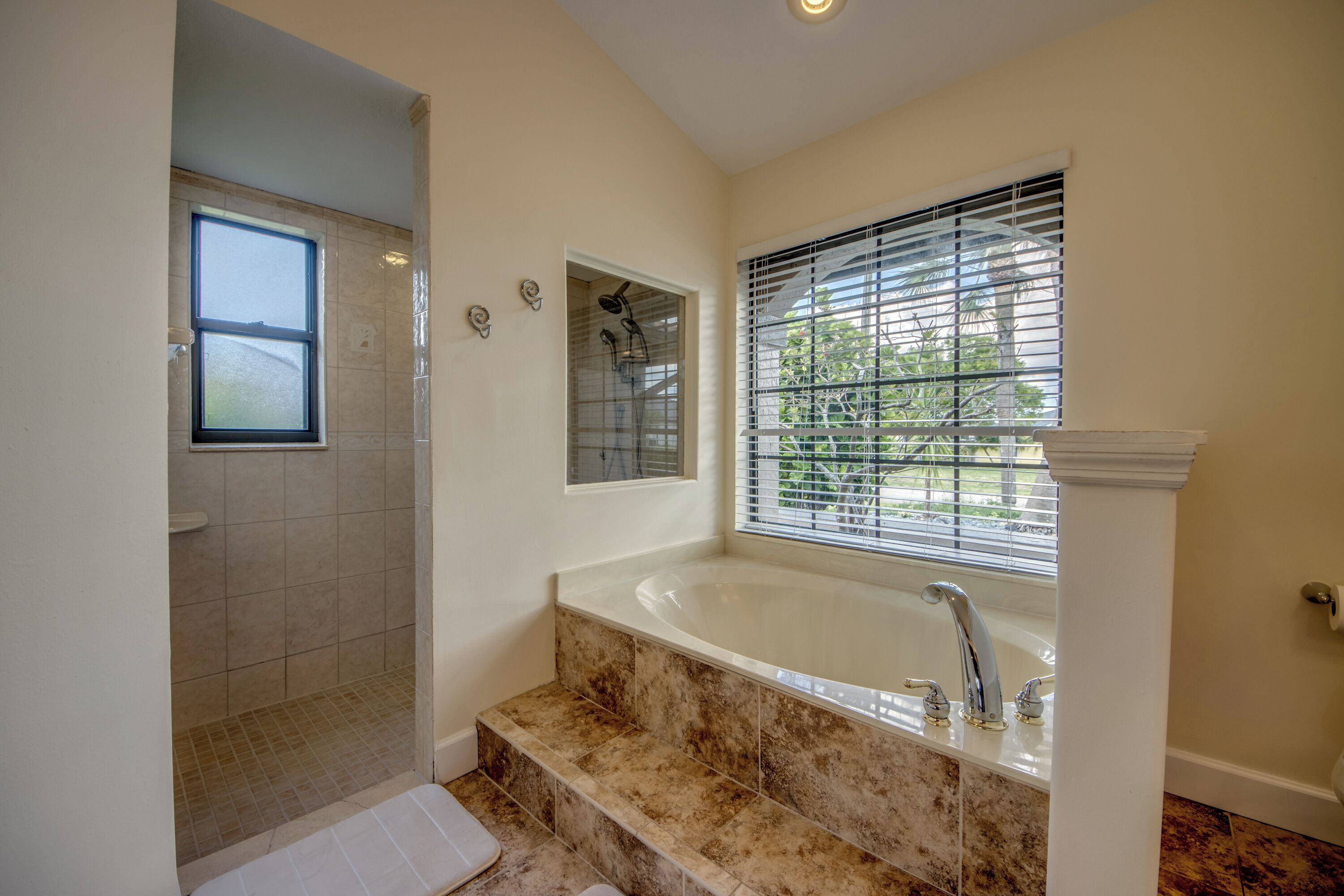 A bathroom with a bathtub, shower, and window with blinds.