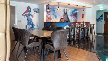 A modern dining area with a long table, multiple chairs, and a bar counter with hanging lights.