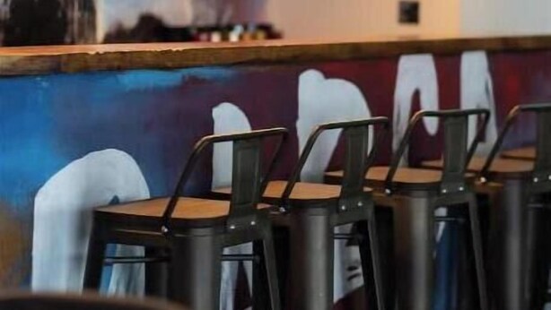 Ein Restaurantinneres mit Metallstühlen, Pendelleuchten und einem Wandgemälde einer Stadtansicht.