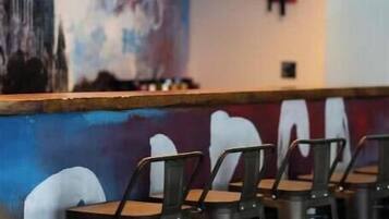 A restaurant interior with metal chairs, pendant lights, and a mural of a cityscape on the wall.