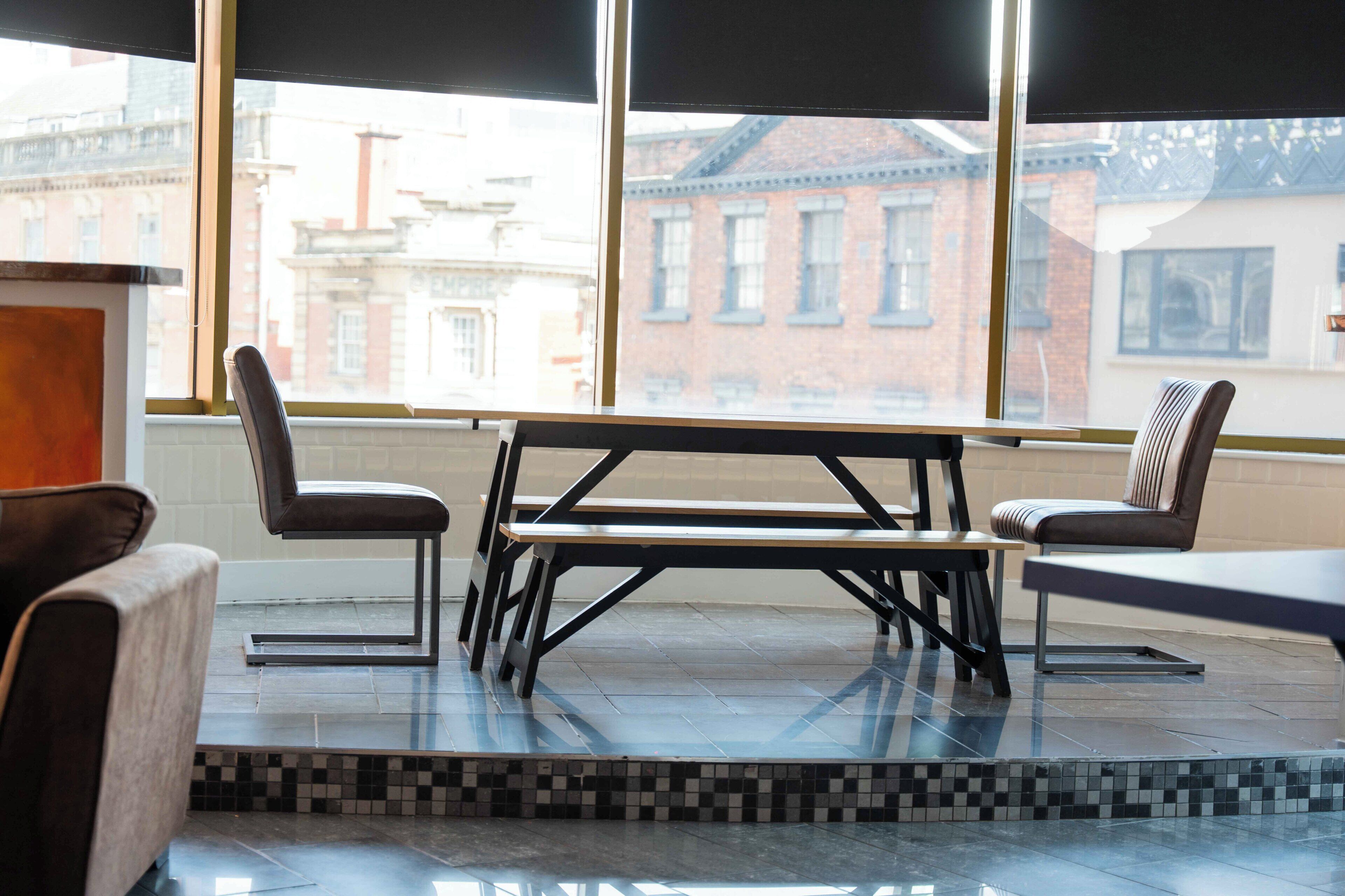 A modern dining area with a table and chairs, large windows with a city view, and a tiled floor.